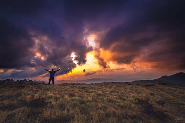 Foto homem de pé no campo contra o céu durante o pôr do sol