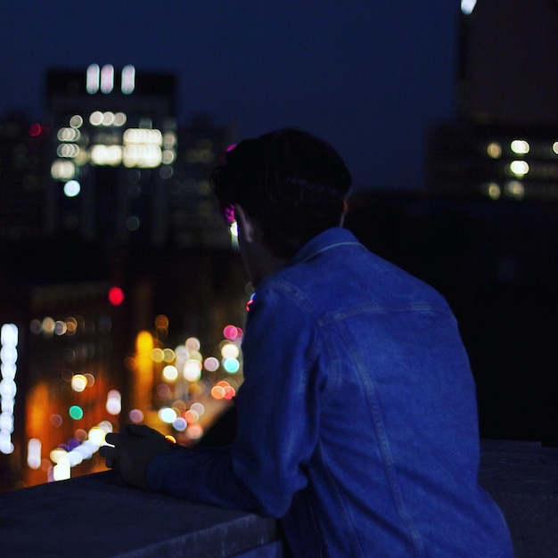 Foto homem de pé no terraço da construção na cidade à noite