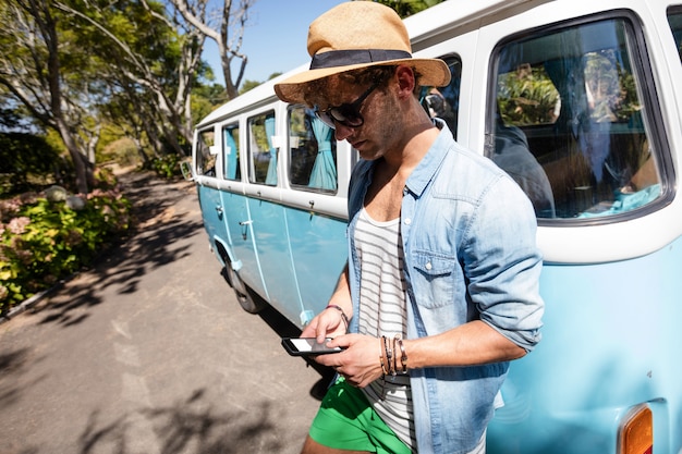 Foto homem de pé perto da caravana e usando telefone celular