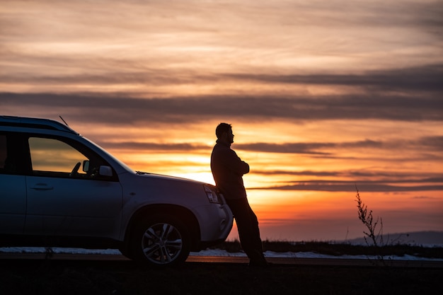 Homem de pé perto do carro, no pôr do sol. conceito de viagens de carro. viagem