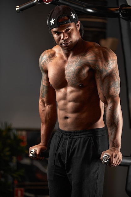 Homem de pele escura forte e musculoso treina em equipamentos modernos no ginásio. Retrato de treinador de fitness muscular bombeado