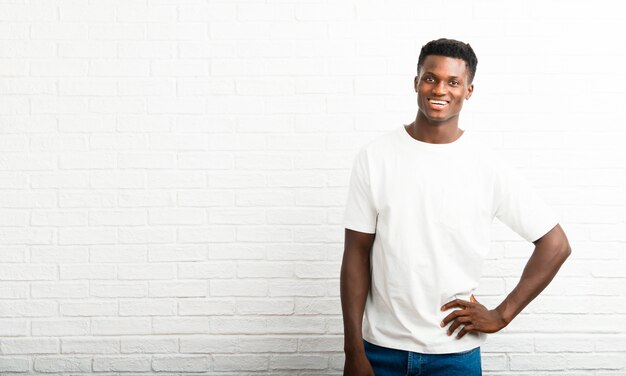 Homem de pele escura posando com os braços no quadril e sorrindo