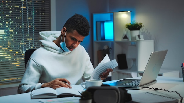 Homem de raça mista com máscara médica assinando documentos em casa, trabalhando à noite