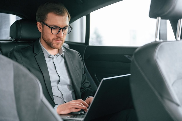 Homem de roupas formais de negócios está sentado no automóvel moderno