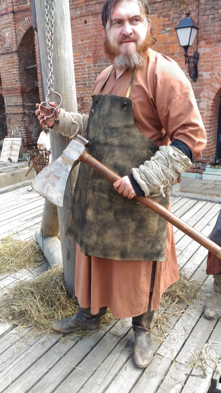 Foto homem de roupas tradicionais segurando um machado enquanto está de pé na fazenda