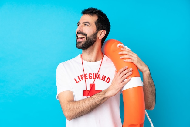 Homem de salva-vidas sobre parede azul isolada feliz e sorridente