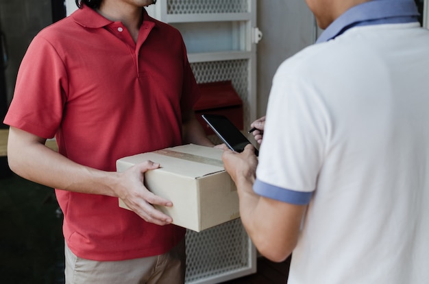 Homem de serviço de entrega em domicílio em uniforme vermelho e assinatura de assinatura de cliente jovem