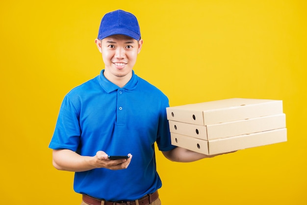 Homem de serviço de entrega sorrindo vestindo uniforme azul segura recipientes de papel para pacotes de caixas de pizza para viagem e mostra smartphone