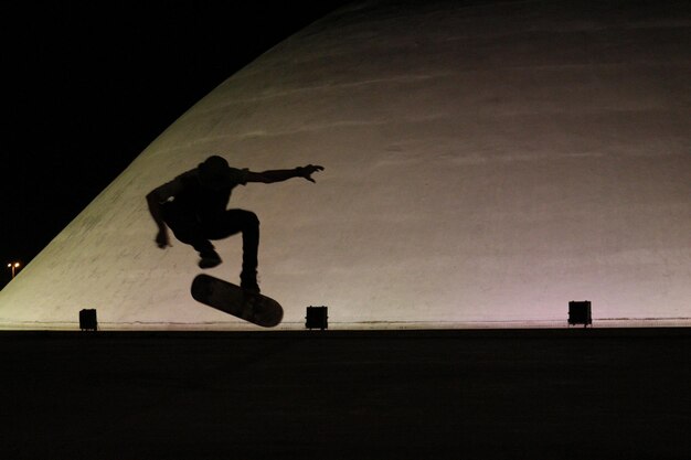 Foto homem de silhueta a saltar de skate à noite.