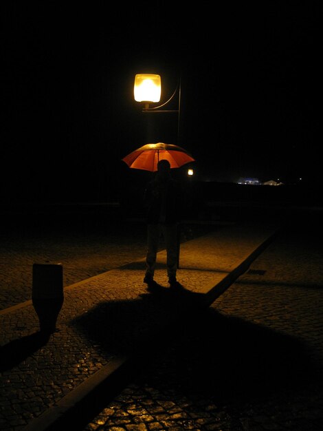 Foto homem de silhueta com guarda-chuva caminhando na rua iluminada à noite