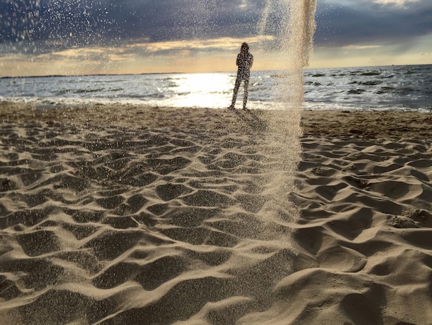 Foto homem de silhueta de pé na praia com areia no ar contra o céu