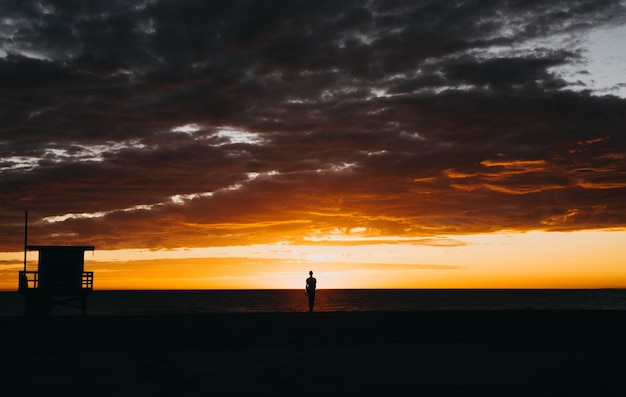 Homem de silhueta de pé na praia contra o céu durante o pôr do sol