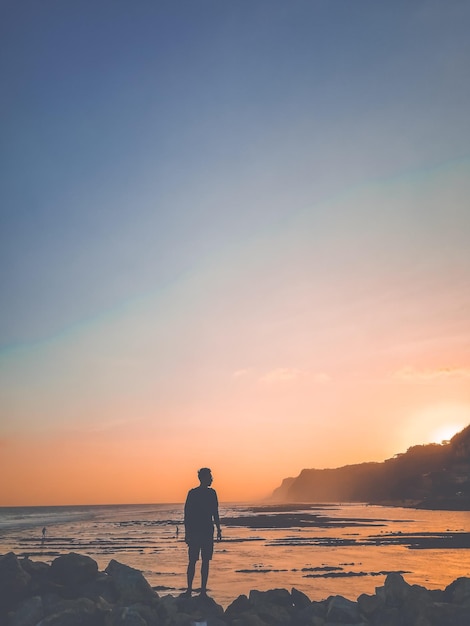 Homem de silhueta de pé na praia contra o céu durante o pôr do sol