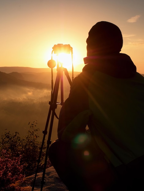 Foto homem de silhueta fotografando câmera contra o céu durante o pôr do sol