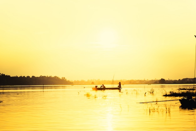 Homem de silhueta no pequeno barco de pesca no lago com vista para a montanha contra o céu do sol