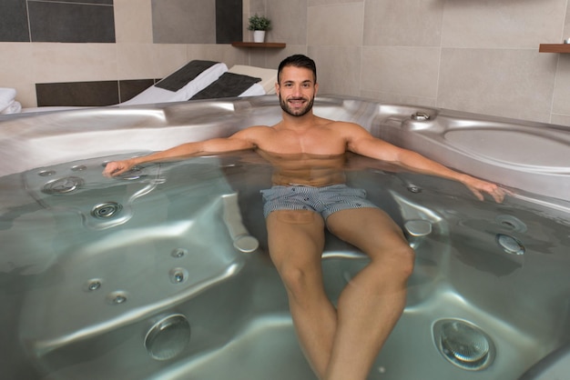 Homem de spa de bem-estar relaxando na banheira de hidromassagem Jacuzzi dentro de casa no retiro de spa de resort de luxo bonito jovem modelo masculino relaxado descansando na água perto da piscina em viagem férias férias