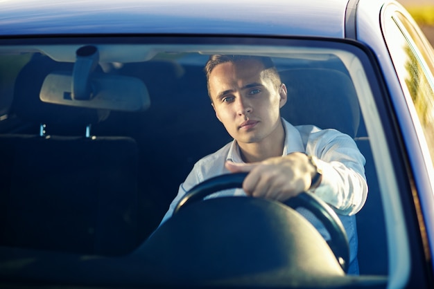 Homem de sucesso bonito atraente na camisa branca, dirigindo um carro caro