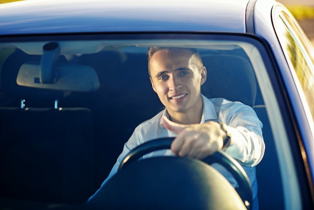 Homem de sucesso bonito atraente na camisa branca, dirigindo um carro caro