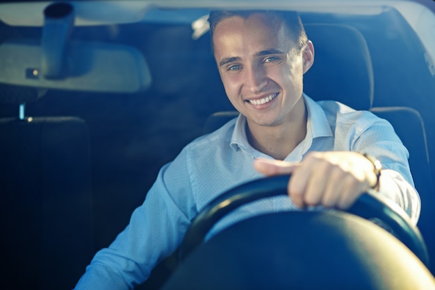 Homem de sucesso bonito atraente na camisa branca, dirigindo um carro caro