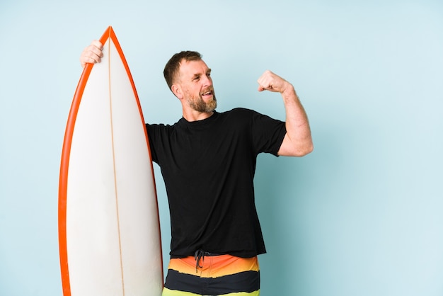 Homem de Surfen isolado na parede azul, levantando o punho após uma vitória, o conceito de vencedor.