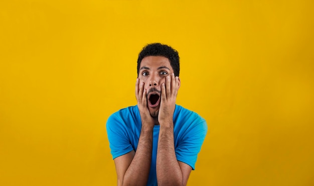 Homem de surpresa isolado em fundo amarelo. Homem negro bonito com camisa azul amarela.