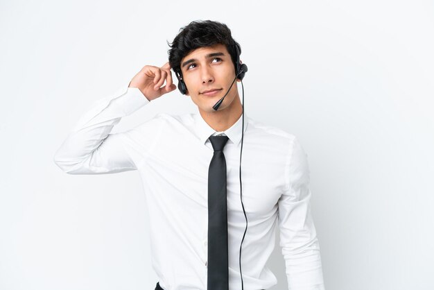 Homem de telemarketing trabalhando com um fone de ouvido isolado no fundo branco com dúvidas e com expressão de rosto confuso