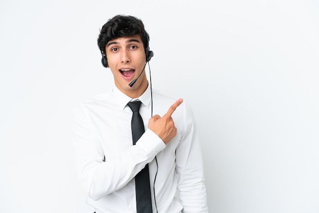 Homem de telemarketing trabalhando com um fone de ouvido isolado no fundo branco surpreso e apontando o lado