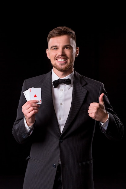 Homem de terno posando com cartas para jogar em fundo preto