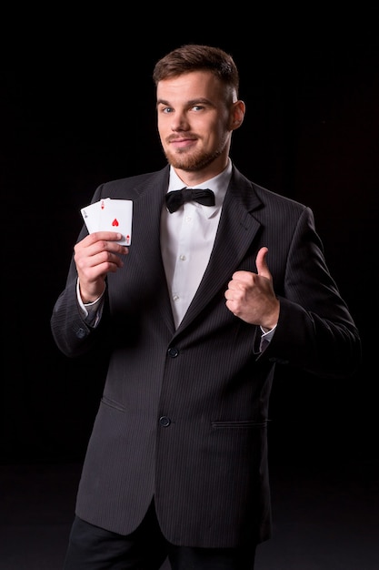 Homem de terno posando com cartas para jogar em fundo preto