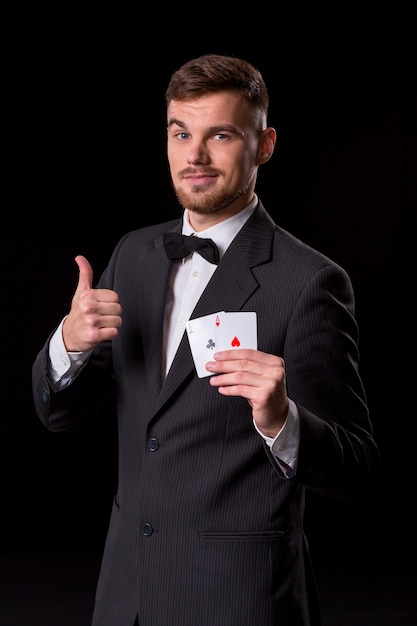 Homem de terno posando com cartas para jogar em fundo preto