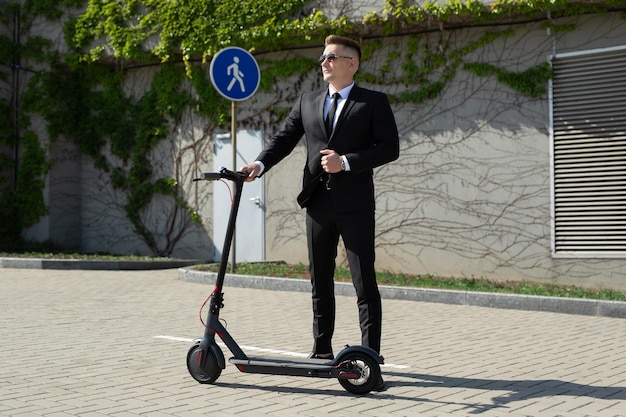 Homem de terno preto fica ao lado de uma scooter elétrica