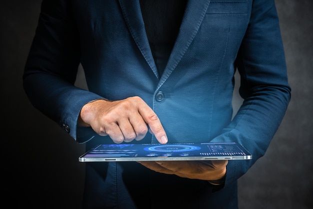 Homem de terno segura tablet digital e toca a tela sensível ao toque com o dedo Empresário segurando o espaço de cópia de fundo escuro do computador tablet