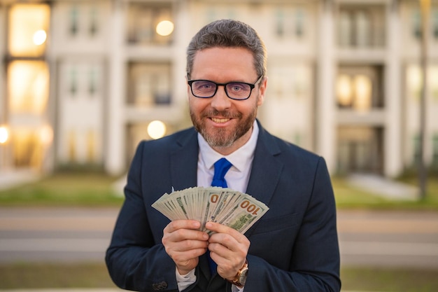 Foto homem de terno segurando dinheiro em notas de dólar retrato ao ar livre de empresário com monte de dol