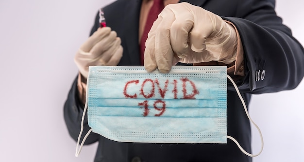 Foto homem de terno segurando máscara protetora médica com o texto covid19. epidemia