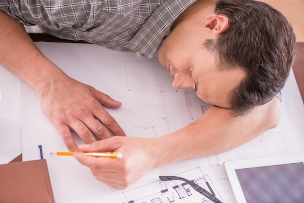 Homem de trabalho cansado que dorme no local de trabalho completamente dos esboços.