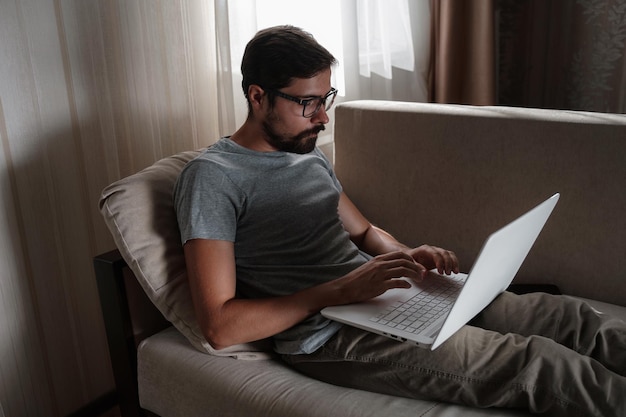 Homem de trabalho remoto trabalhando no laptop sentado no sofá em casa