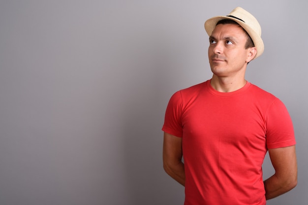Homem de turista usando chapéu e camisa vermelha contra parede cinza