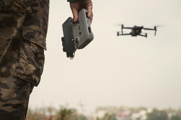 Homem de uniforme militar com um painel de controle UAV em suas mãos um drone voando no fundo em