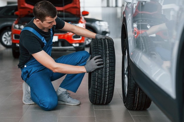 Homem de uniforme trocando pneu de automóvel Concepção de serviço de carro