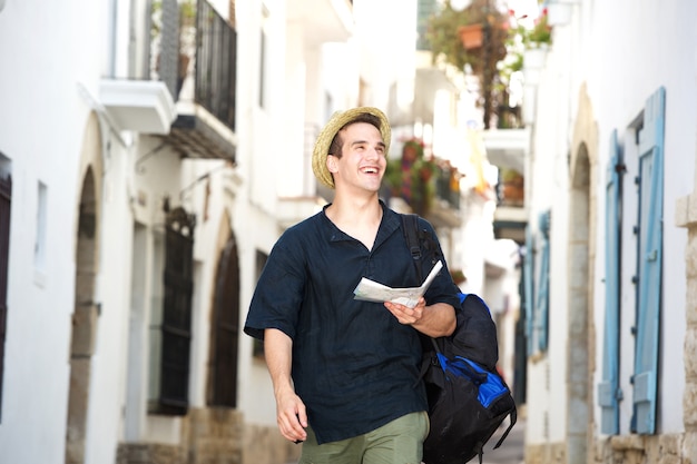 Homem de viagem sorridente andando na cidade com bolsa e mapa