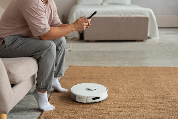 Homem de vista lateral com aspirador robótico em casa