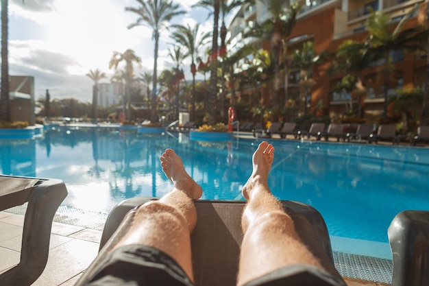 Homem deita-se e descansa numa espreguiçadeira perto da piscina com palmeiras ao pôr-do-sol férias na ilha da madeira hotel e spa pernas masculinas