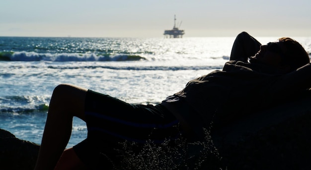 Foto homem deitado em uma rocha na costa do mar contra o céu