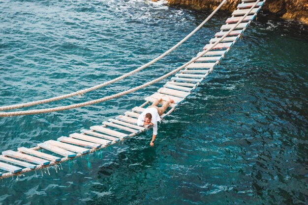 Homem deitado na ponte suspensa, apreciando a vista para o mar e a calma da natureza