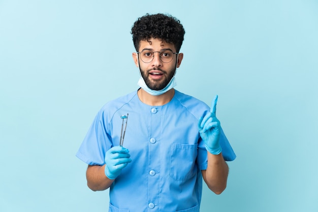 Homem dentista marroquino segurando ferramentas isoladas em azul com a intenção de descobrir a solução enquanto levanta um dedo