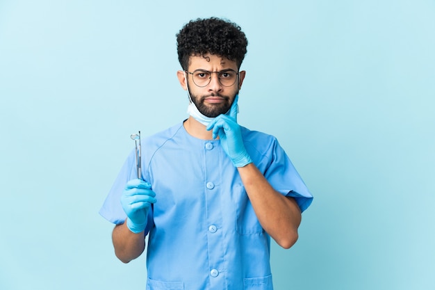 Homem dentista marroquino segurando ferramentas isoladas, tendo dúvidas e pensando