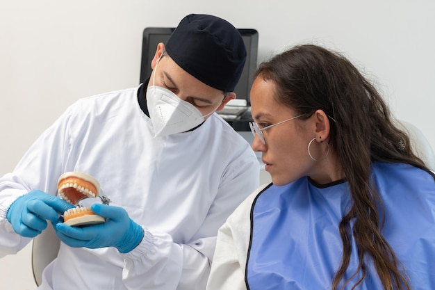 Homem dentista segurando um modelo odontológico dando uma explicação a um paciente