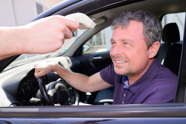 Homem dentro de um carro, medindo sua temperatura