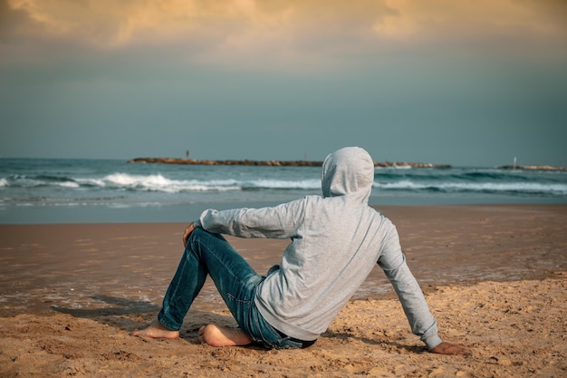 Homem descalço sentado na praia e olhando para o mar