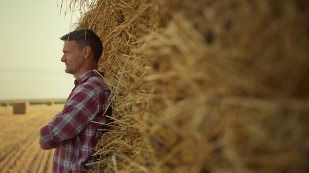 Homem descansa pilha de feno no campo agrícola Agricultor pilha de trigo seco magro no outono